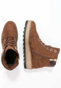 Brązowe zamszowe botki sięgające kostki o fakturowanej powierzchni, z bocznym zamkiem błyskawicznym, okrągłymi sznurówkami i grubą czarną gumową podeszwą.