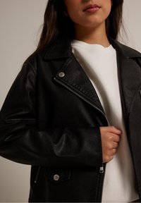 Giacca biker in ecopelle nera con accessori in argento, chiusura con zip e colletto a rever. Presenta una tasca con zip e un fit rilassato.