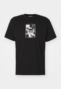 Črna bombažna majica s kratkimi rokavi, ki vsebuje bel grafični dizajn živali, ki kadi pijano na sprednji strani. Standardni krojač s krožnim ovratnikom.