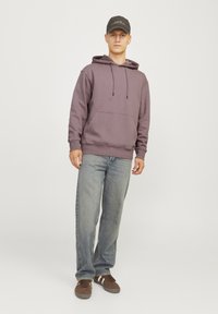 Purple hooded sweatshirt with drawstrings, kangaroo pocket, and ribbed cuffs, paired with light blue denim jeans and brown sneakers.