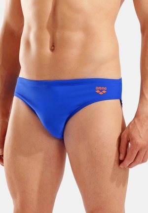 Torace maschile che indossa slip da nuoto blu del marchio Arena con logo arancione sul lato destro, su sfondo bianco.