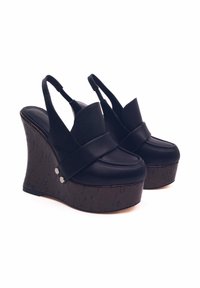 Scarpe con zeppa nera dal design slingback, parte superiore in pelle, fascia ampia e base testurizzata simile al sughero. Presentano borchie di accento argentate.