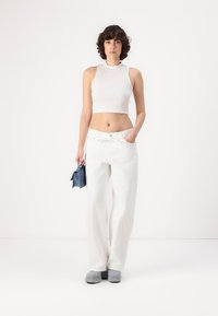 Bílý crop top a volné bílé kalhoty. Šedé platformové boty a malá modrá taška. Hladká textura; minimalistický design.
