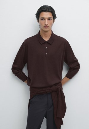 Burgundowa koszulka polo z długim rękawem, z trzema guzikami; faktura ribbed; zestawiona z ciemnymi spodniami i teksturowanym swetrem przewiązanym w talii.
