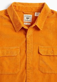 Camicia in corduroy di un vivace arancione con vestibilità rilassata, dotata di colletto a punta, due tasche sul petto e bottoni arancioni.