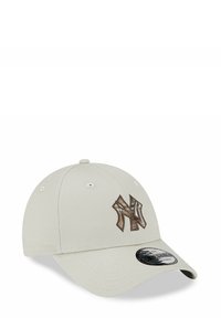 Gorra de béisbol beige claro con un logo marrón texturizado en la parte frontal, con visera curva y agujeros de ventilación a los lados.