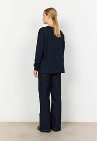 Navy blue sweatshirt with a relaxed fit, ribbed cuffs, and a slightly longer back. Paired with dark blue wide-leg denim pants.