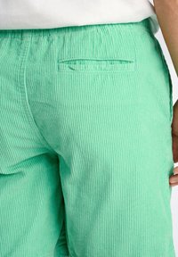 Pantaloni in velluto a coste verde con una texture rigata e una tasca posteriore. Il tessuto presenta una finitura morbida e un design dalla vestibilità rilassata.