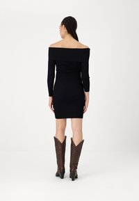 Vestido preto com nervuras, de ombros à mostra, com mangas longas, silhueta ajustada e comprimento até ao joelho, combinado com botas de cowboy castanhas com detalhes em relevo.