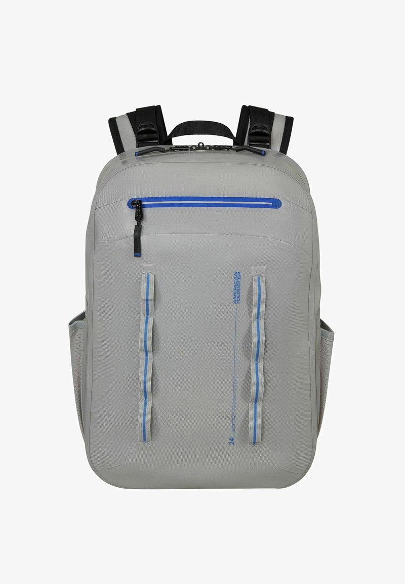 Sac à dos gris clair avec fermeture éclair bleue, double sangles verticales, bretelles rembourrées et poches latérales en mesh, conçu pour un usage quotidien.