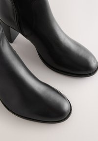 Bottes de cheville en cuir noir avec un bout pointu, une couture discrète et un talon bloc. Texture lisse avec un design élégant.