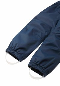 Marina vattentäta overaller med elastiska muddar, med vita öglor för enkel påtagning. Slät syntetisk textur med en avslappnad, lös passform.