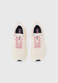 Light beige athletic shoes with pink laces, textured upper, and dark navy accents on the sole and insole. Features a breathable design.