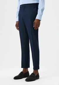 Marineblauwe pantalon met een gestructureerde stof, slim fit, taps toelopende pijpen en omgeslagen boorden. Voorzien van een riemlus en een sluiting met één knoop.