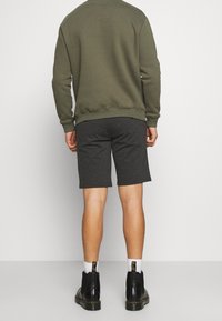 Felpa verde oliva con vestibilità rilassata, abbinata a pantaloni corti grigio scuro. Il modello indossa stivaletti neri alla caviglia e calzini bianchi.
