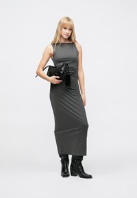 Rochie maxi gri, elegantă, cu siluetă ajustată, fără mâneci și detaliu adunat în talie. Asortată cu o geantă mică, lucioasă, de culoare neagră.