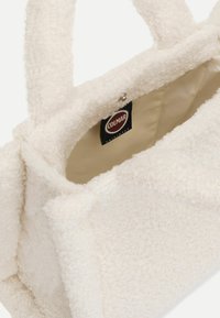 Fehér, textúrált kézitáska puha, bolyhos anyagból, két rövid fogantyúval és bézs belső résszel. Tartalmazza a "Colmar Originals" címkét belül.