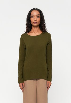 Olijfgroene top met lange mouwen, ronde hals en een zachte, gestructureerde stof. Gecombineerd met beige wijde broek staat het model tegen een witte achtergrond.