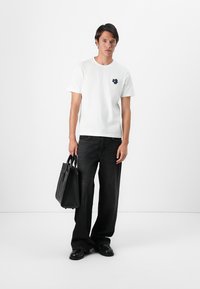 White cotton t-shirt with a navy blue floral logo, paired with high-waisted black denim jeans and a black leather tote bag.