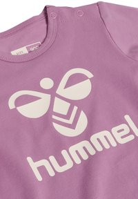 Lilla bomulds T-shirt med et stort hvidt bi-logo og teksten "hummel." Rund halsudskæring med trykknapper på skulderen for nem påklædning.