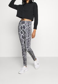 Felpa nera corta con orlo regolabile, abbinata a legging aderenti con un motivo a serpente in bianco e nero. Sneakers bianche indossate.