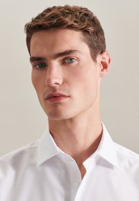 Witte button-up shirt met een klassieke kraag, met een gladde stoftextuur en een aansluitend ontwerp, gedragen door een persoon met kort haar.