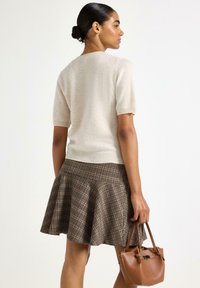 Beige kortærmet sweater parret med en brun ternet flared nederdel, som holder en lille brun lædertaske. Glat tekstur med en tætsiddende silhuet.