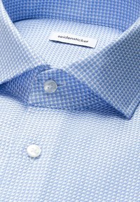 Nahaufnahme eines hellblauen Hemdkragens mit Muster, weißen Knöpfen und einem "seidensticker" Etikett im Inneren des Kragens.