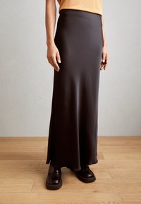 Lange zwarte satijnen rok met een gladde textuur en een lichte flair aan de zoom. Gepaard met donkere, chunky schoenen, gestyled met een licht topje.