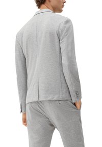 Grijze blazer van gestructureerde stof, met een enkele split, notch-revers en knopenmanchetten. Gecombineerd met een bijpassende grijze broek.