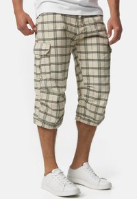 Shorts cargo à carreaux beiges, de coupe mi-genou, avec des poches latérales et des lignes noires en grille. Fabriqués dans un mélange de coton léger.