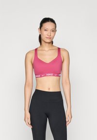 Nike sportmelltartó élénk rózsaszínben, V-nyakkivágással és széles pántokkal, fehér logós rugalmas szalaggal. Magas derekú fekete leggingsszel viselve.