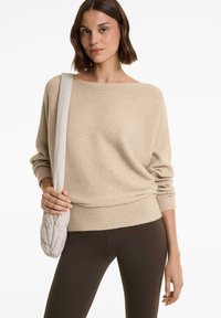 Beige, bordázott pulóver, széles dekoltárral és laza szabással, sötétbarna leggingssel és világos steppelt válltáskával párosítva.