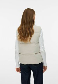 Beige gewatteerde vest met verticale geribde textuur, gedragen over een langslavend wit top. De achterkant heeft een eenvoudig ontwerp met een lichte curve aan de zoom.