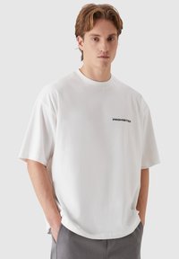 White cotton t-shirt with short sleeves, featuring a black "PROHIBITED" text on the chest. Loose fit with a round neckline.