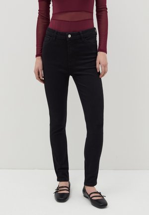 Jeans skinny negros con cintura de altura media, cierre de botón y dos bolsillos frontales, combinados con unos zapatos tipo Mary Jane negros y una blusa de gasa burdeos.
