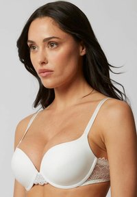 White bra featuring molded cups, lace band detail, adjustable straps, and a smooth finish. Focus on comfort and support.