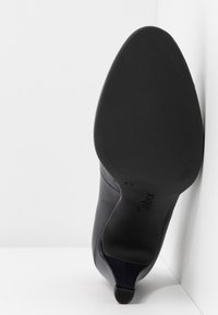 Černá kožená lodička s špičatou špičkou a nízkým podpatkem, texturovaná podešev a označení velikosti 4½, umístěná vztyčeně proti bílým plochám.