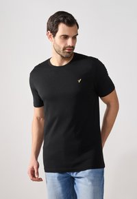Svart bomulls t-skjorte med korte ermer og rund hals, med en liten gullfugl-logo på brystet. Glatt tekstur med en tettsittende design.