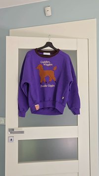 Fialová mikina s grafikou hnědého pudla a textem "Objímání, vrtění, pudlové smíchy." Obsahuje kontrastní hnědý výstřih a manžety.