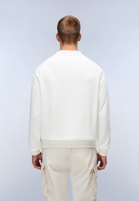 Felpa bianca con un fit rilassato e polsini a coste, abbinata a pantaloni cargo beige. Il tessuto sembra morbido e con una texture liscia.
