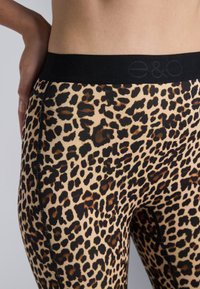 Leggingy s uzorkom leoparda s crnim strukom, koja imaju glatku teksturu i kontrastnu crnu šav na stranama.