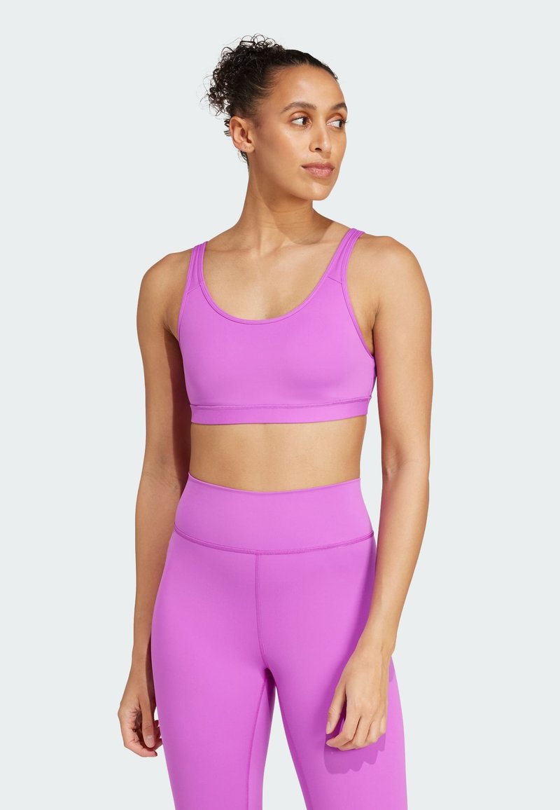 Sujetador deportivo morado con tirantes anchos, textura suave y un diseño ajustado, combinado con leggings de cintura alta a juego en el mismo color.
