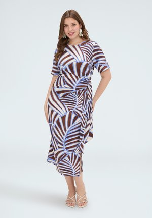 Lachende vrouw die een midi-jurk met korte mouwen draagt met een blauw en bruin abstract bladpatroon en beige sandalen met bandjes.