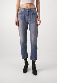 Jeans de mezclilla azul claro con corte recto, ligero desteñido, diseño de cinco bolsillos y dobladillo sin rematar. Combinados con botines negros hasta el tobillo.