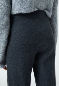 Leggings gris foncé en maille côtelée avec une texture lisse, dotées d'une taille haute et d'une silhouette ajustée, associées à un pull gris clair.