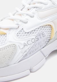 Lacoste tennis jalanike, millel valge sünteetiline ja võrkmaterjal, halli seemisnahast detailidega ning tekstureeritud tallaga. Kaasas on nöörid ja logo detail.