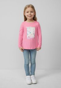 Rosa Langarmshirt mit einem Einhorn-Design und dem Aufdruck "TRÄUME". Kombiniert mit hellblauen Skinny-Jeans und weißen Sneakers.