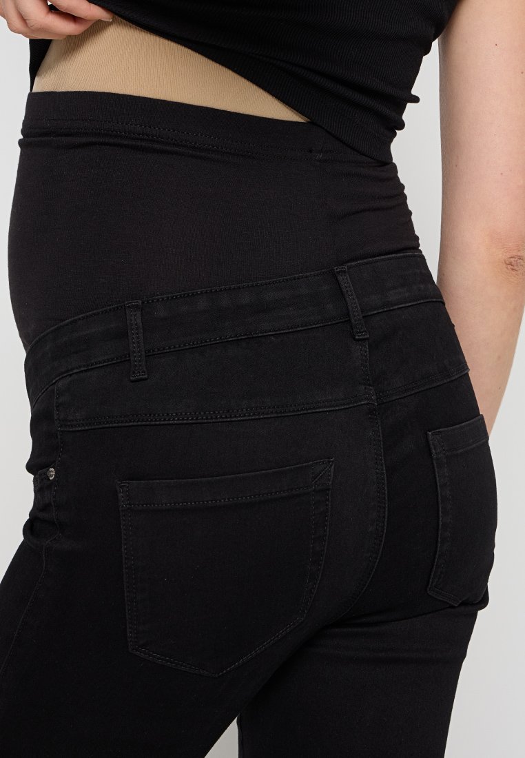 Schwarze hochtaillierte Jeans mit glatter Textur, ausgestattet mit Gesäßtaschen und dezenten Stichdetails. Sichtbare überlappende schwarze Hemdenschicht.