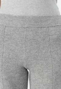 Leggings grigi in maglia con una cintura a coste, caratterizzati da una texture liscia e dettagli di cucitura. Il materiale sembra morbido e elasticizzato.